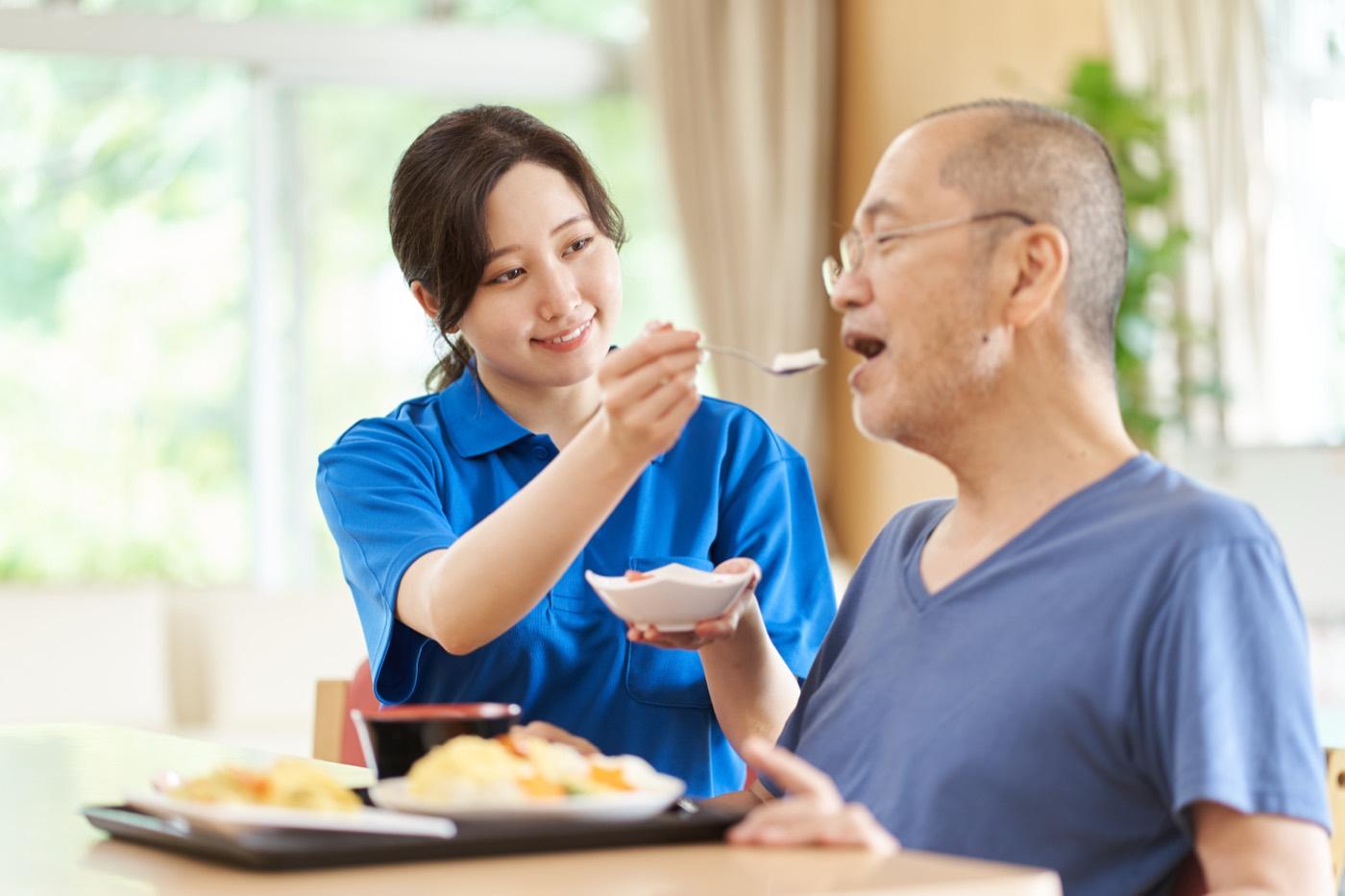 A caregiver helps an older man enjoy a home-cooked meal.
